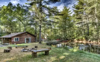 a cabin in the woods with a pond and benches at Cozy Cottage Rental with Small Private Pond in Canadensis, Pennsylvania in Canadensis