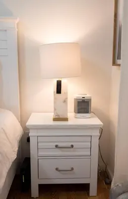 a white nightstand with a lamp and a clock on it at Lovely 1 bedroom apt with patio by Yankee Stadium in Melrose