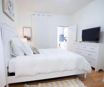 a white bedroom with a white bed and a flat screen tv at Lovely 1 bedroom apt with patio by Yankee Stadium in Melrose