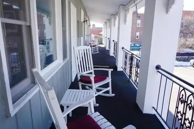 two white chairs sitting on a porch next to windows at Stay Saratoga in Saratoga Springs
