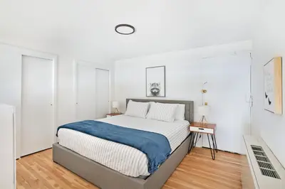 a white bedroom with a large bed with a blue blanket at Amazing Apartment for 2 1 Bed 1 Bath in New York