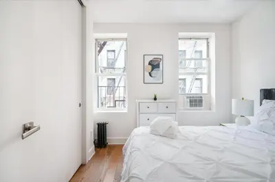 a white bedroom with a large bed and two windows at 1 BR Gem in Prime Location of NYC in New York