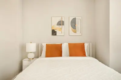 a white bedroom with a white bed with orange pillows at Gorgeous Studio Apartment in New York