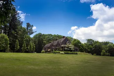 a large house on a green field with trees at Inn at Lake Joseph in Forestburgh