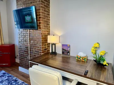 a living room with a desk with a tv on a brick wall at BP STAYS - Hotel-Style, No Host, Professionally Managed ID265 in Jersey City