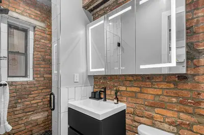 a bathroom with a white sink and a brick wall at Modern Nolita Hideaway in New York