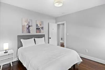 a white bedroom with a large bed and a nightstand at Owl's Nest - 5BR apartment in New Haven