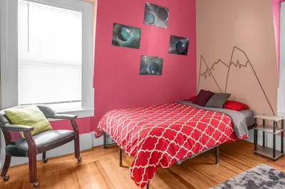 a bedroom with a red wall with a bed and a chair at Enchanting 3BR Near Downtown Hartford Cozy & Modern with Parking in Hartford