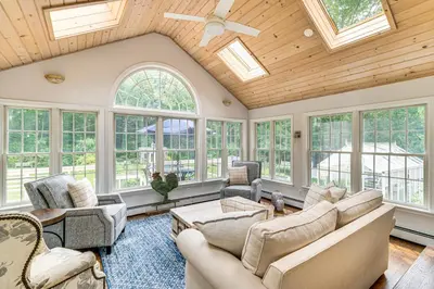 a living room with a vaulted ceiling with windows at Pool, Sunroom and Gardens Luxe Sandy Hook Home!