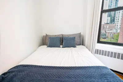 a bedroom with a bed with blue pillows and a window at Chic 2BD Upper East Side Retreat in New York