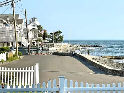 a road next to the ocean with a white fence at Dog-Friendly Oceanfront Getaway - Walk to Dining - Private Beach Access in Milford