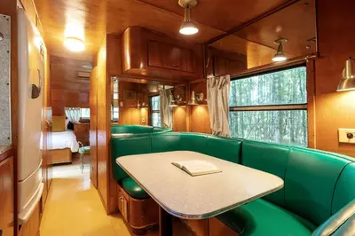 a train room with a table and green seats at Gorgeous Fully Restored Caravan Nestled in the Trees Along Silver Lake for a Unique Vacation in Woodridge, New York in Woodridge