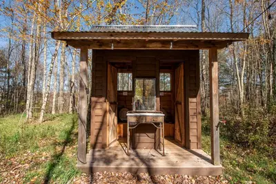 a small out house in the middle of a forest at Gorgeous Fully Restored Caravan Nestled in the Trees Along Silver Lake for a Unique Vacation in Woodridge, New York in Woodridge