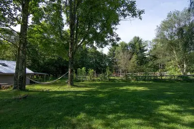 a yard with a fence and a tree with a hammock at Gorgeous Fully Restored Caravan Nestled in the Trees Along Silver Lake for a Unique Vacation in Woodridge, New York in Woodridge