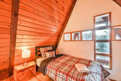 a bedroom in a log cabin with a bed and windows at Triangle Tranquility Unique A Frame 6 BR Home in Lanesville