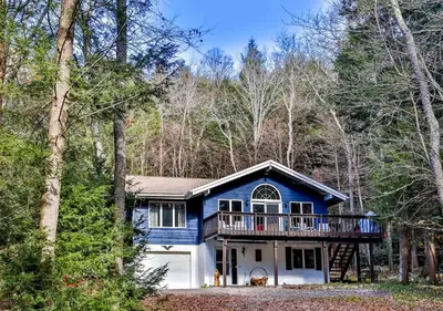 a blue house with a deck in the woods at Secluded Retreat w Hot Tub in Windham in Windham