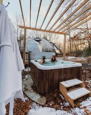 two people sitting in a hot tub in a backyard at Unique Dome Home With Hot Tub & Piano, on 28 acres in New Paltz