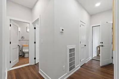 a bathroom with white walls and wooden floors and a toilet at NYC Edge Triplex Full House | Parking & Near Shops in North Bergen
