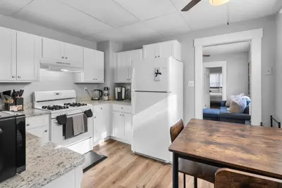 a kitchen with white cabinets and a table and a refrigerator at Sunny Room Steps from SCSU in New Haven
