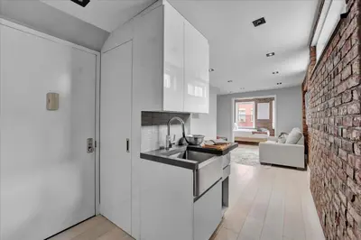 a kitchen with white cabinets and a brick wall at SoHo Designer 2BR w balcony in New York