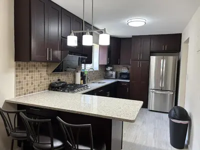 a kitchen with wooden cabinets and a island with bar stools at NYC Bayside LIRR Cozy Suite in Bayside