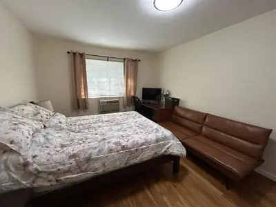 a bedroom with a bed and a couch and a window at NYC Bayside LIRR Cozy Suite in Bayside