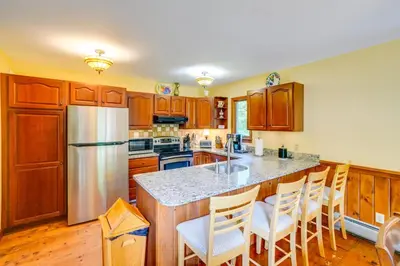 a kitchen with wooden cabinets and a kitchen island with bar stools at Game Room, Hot Tub! Year-Round Dover Retreat in West Dover
