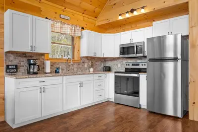 a kitchen with white cabinets and a stainless steel refrigerator at Luxury Log Cabin Lakefront, Game room & Fire Pit, in Schenevus