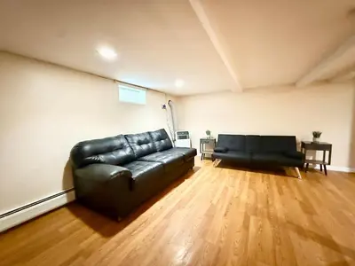 a living room with a black leather couch and wooden floors at Charming Milford Montague Riverway Cottage in Montague