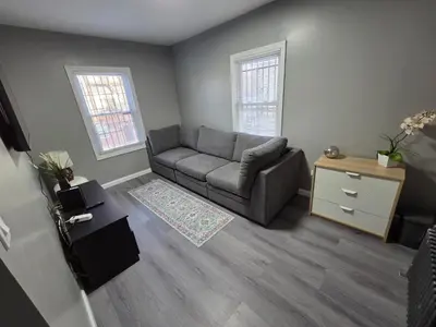 a living room with a gray couch and two windows at Grand Central & Times Square in 25-30 mins!! in Corona