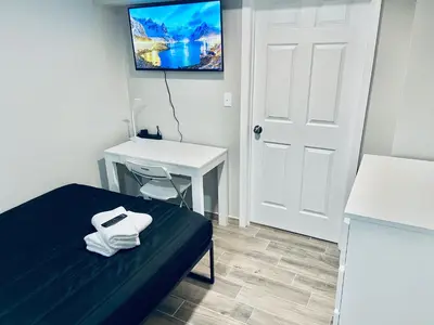 a room with a bed and a desk and a tv at Bright, Stylish and Comfortable Room with Workspace! in Haledon