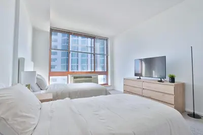 a white bedroom with two beds and a flat screen tv at Hudson River waterfront apt w sweeping NYC views in Hoboken