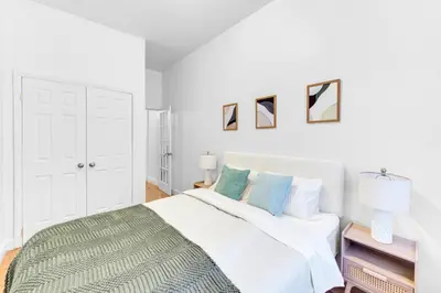 a white bedroom with a large white bed with blue pillows at Inviting 2Bd Upper East Side Stay with Backyard in New York
