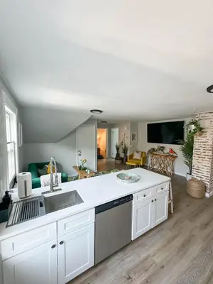 a kitchen with white cabinets and a living room at The Nest At Elm City Flats in New Haven