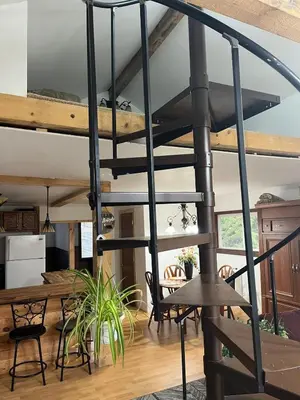 a metal spiral staircase in a living room with a table at Adirondack Trailside Cabin in Caroga Lake