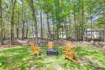 three chairs and a table in a yard with trees at Family Cabin with Hot Tub Game Room Tobyhanna in Tobyhanna