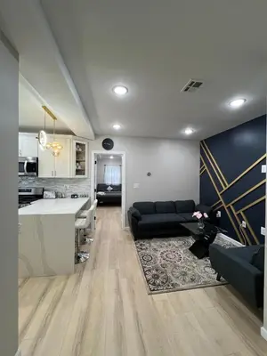 a living room with a black couch and a kitchen at Modern 2BR and Office Near NYC With Parking - Sleeps 6 in Jersey City