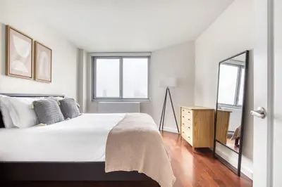 a white bedroom with a large bed and a mirror at Blueground Murray Hill balcony nr East River NYC-720 in New York