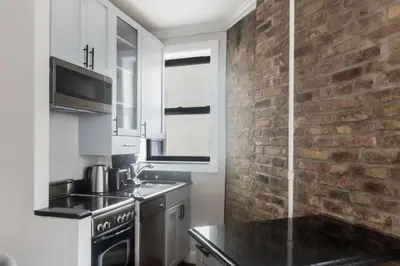 a kitchen with white cabinets and a brick wall at Blueground Nolita private entrance nr Bowery NYC-2054 in New York