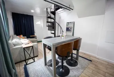 a living room with a table and a spiral staircase at Bright 1-Bedroom Loft in Converted Garage with Private Entrance in New Rochelle