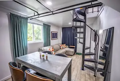 a living room with a staircase and a table and chairs at Bright 1-Bedroom Loft in Converted Garage with Private Entrance in New Rochelle