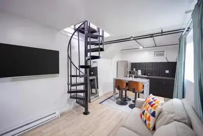 a living room with a spiral staircase and a kitchen at Bright 1-Bedroom Loft in Converted Garage with Private Entrance in New Rochelle