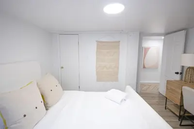 a white bedroom with a white bed and a desk at Retro 2 bedroom basement APT with free parking in New Rochelle