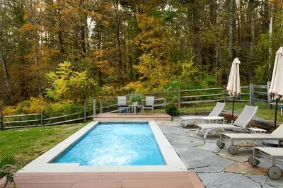 a swimming pool with chairs and umbrellas in a yard at Elegant 7BR Estate with Pool & Hot Tub in Berkshires in North Egremont