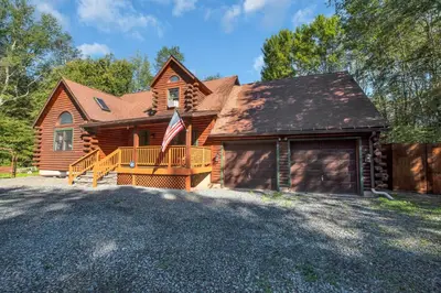 a log home with a flag on a driveway at Secluded Log Cabin with Hot Tub Fire Pit Game Room in Newfoundland