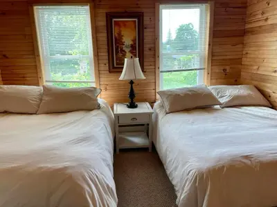 two beds in a room with wooden walls and windows at The Mountain House in Lanesville
