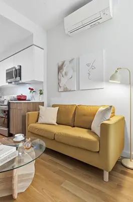 a living room with a yellow couch and a kitchen at Elegant Studio Apartment in Steinway