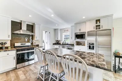 a kitchen with white cabinets and a large island with chairs at 8 Mi to Jiminy Peak Resort Mtn-View Home with Deck in Stephentown