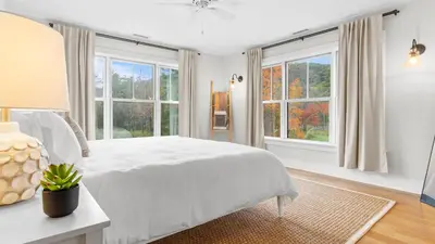 a white bedroom with a large bed and windows at Modern Berkshires Farmhouse w Porch Fireplace Views Beaver Creek by AvantStay in Stockbridge