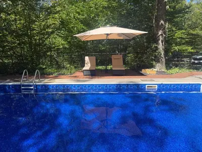 a blue swimming pool with an umbrella and two chairs at Blue Bird Chalet 5BR with Sauna near Skiing in East Chatham